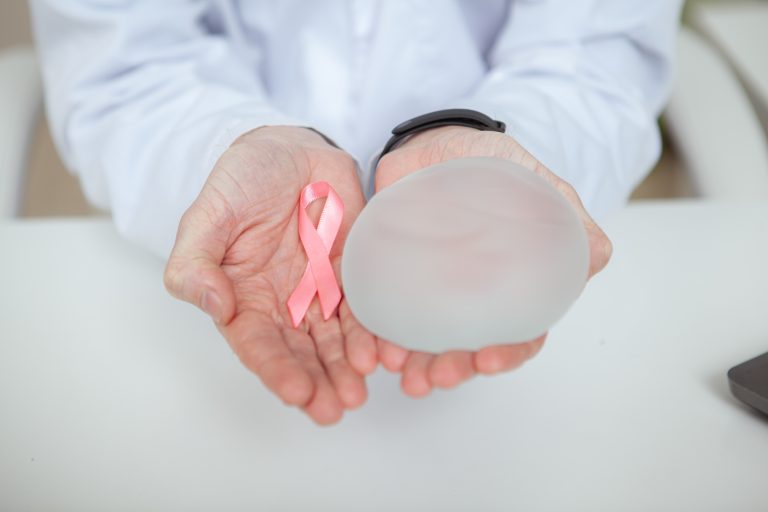 Plastic surgeon holding silicone breast implant and pink ribbon